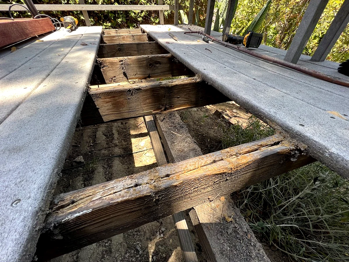 Screwdriver tip sinking into a soft, rotted section of a deck post near ground level